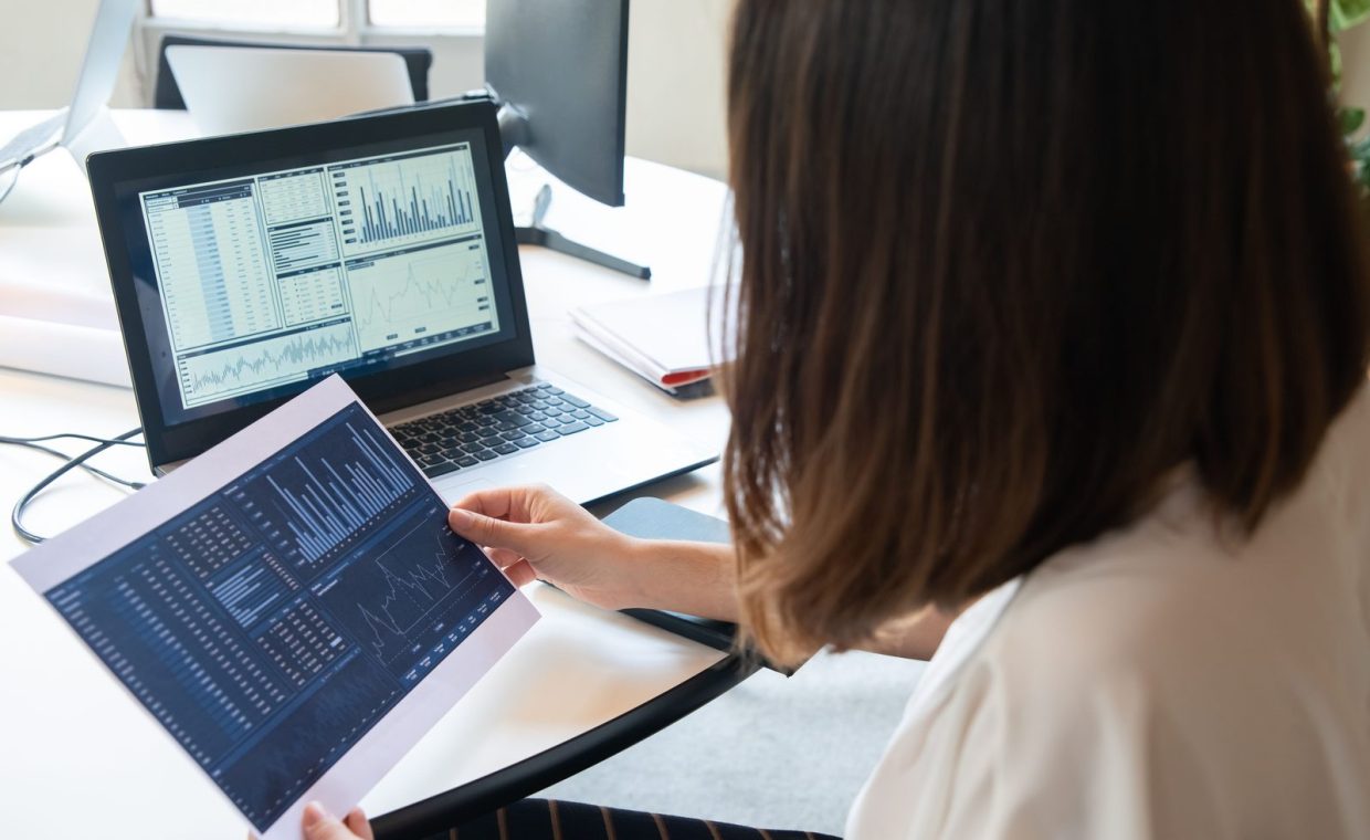 A professional woman analyzes financial charts on a laptop and paper for business insights.