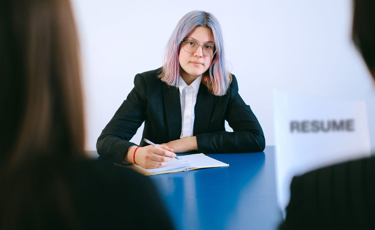 A young woman with dyed hair takes notes during a job interview.