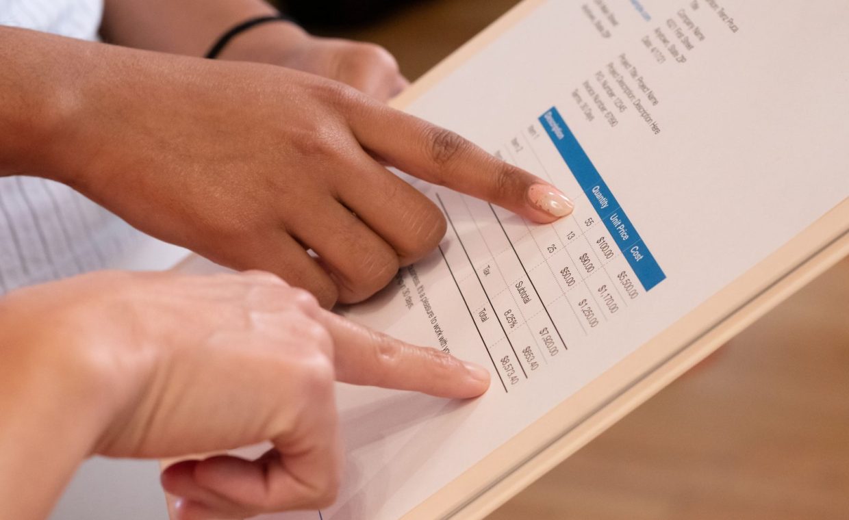 Two people pointing at financial details on a document, highlighting invoice analysis.