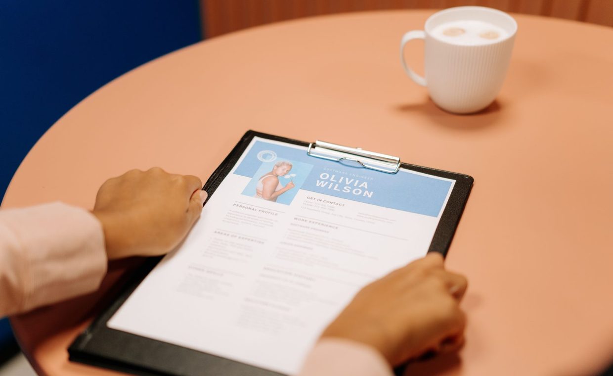 Close-up of hands holding resume during interview with coffee on table, highlighting workplace setting.