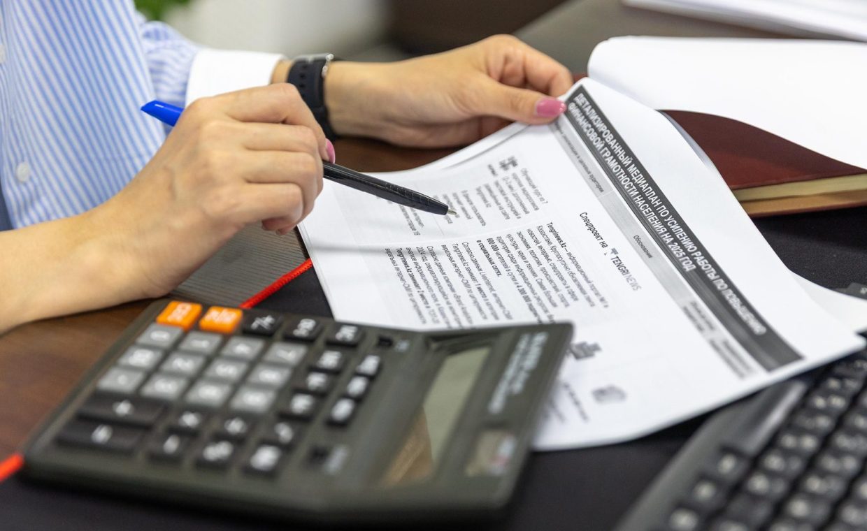 Close-up of a person analyzing financial documents using a calculator and pen.
