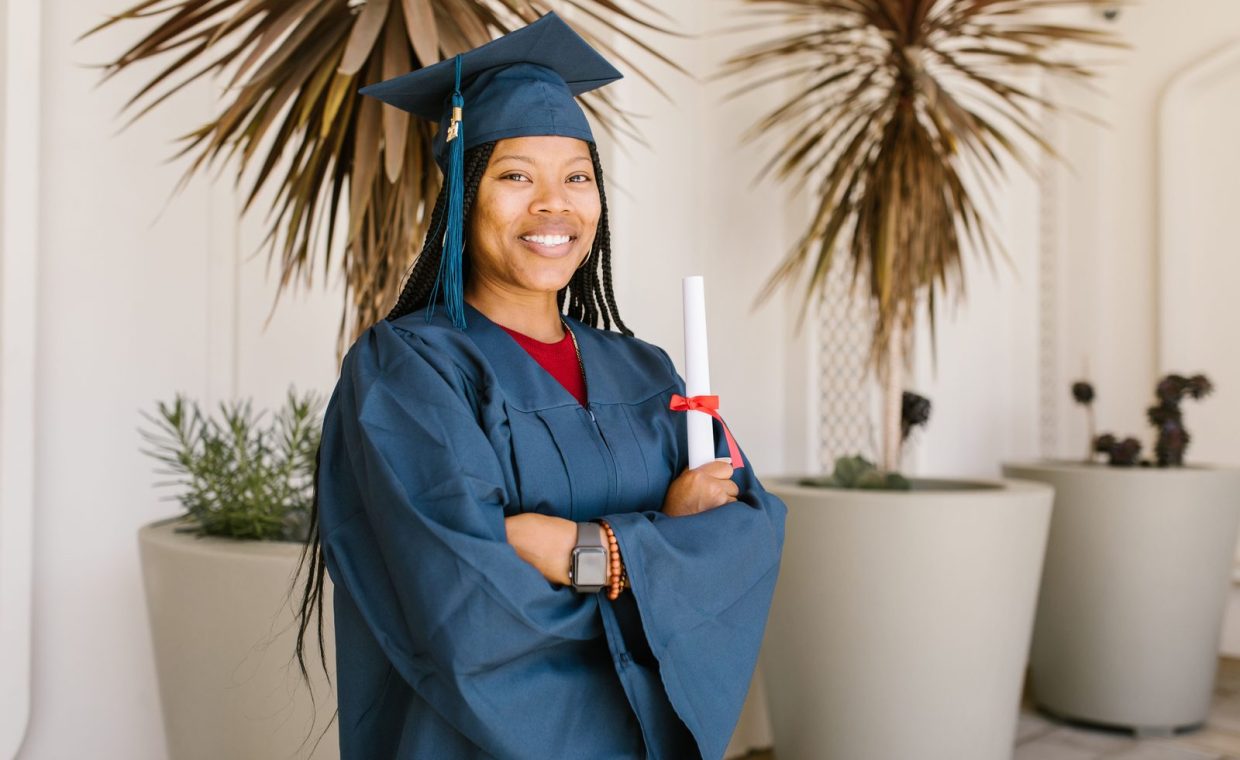 Smiling young woman in graduation gown holding diploma indoors.