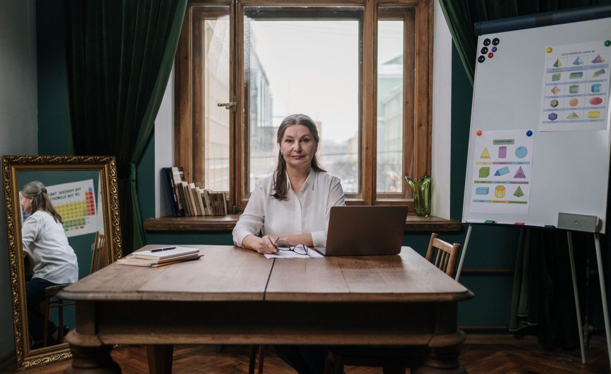 Elderly woman teaching with laptop in home office, showcasing charts and educational materials.