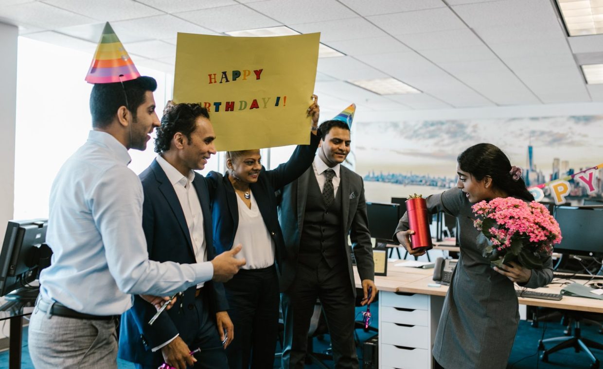 Colleagues surprise a coworker with a birthday celebration in a modern office setting.