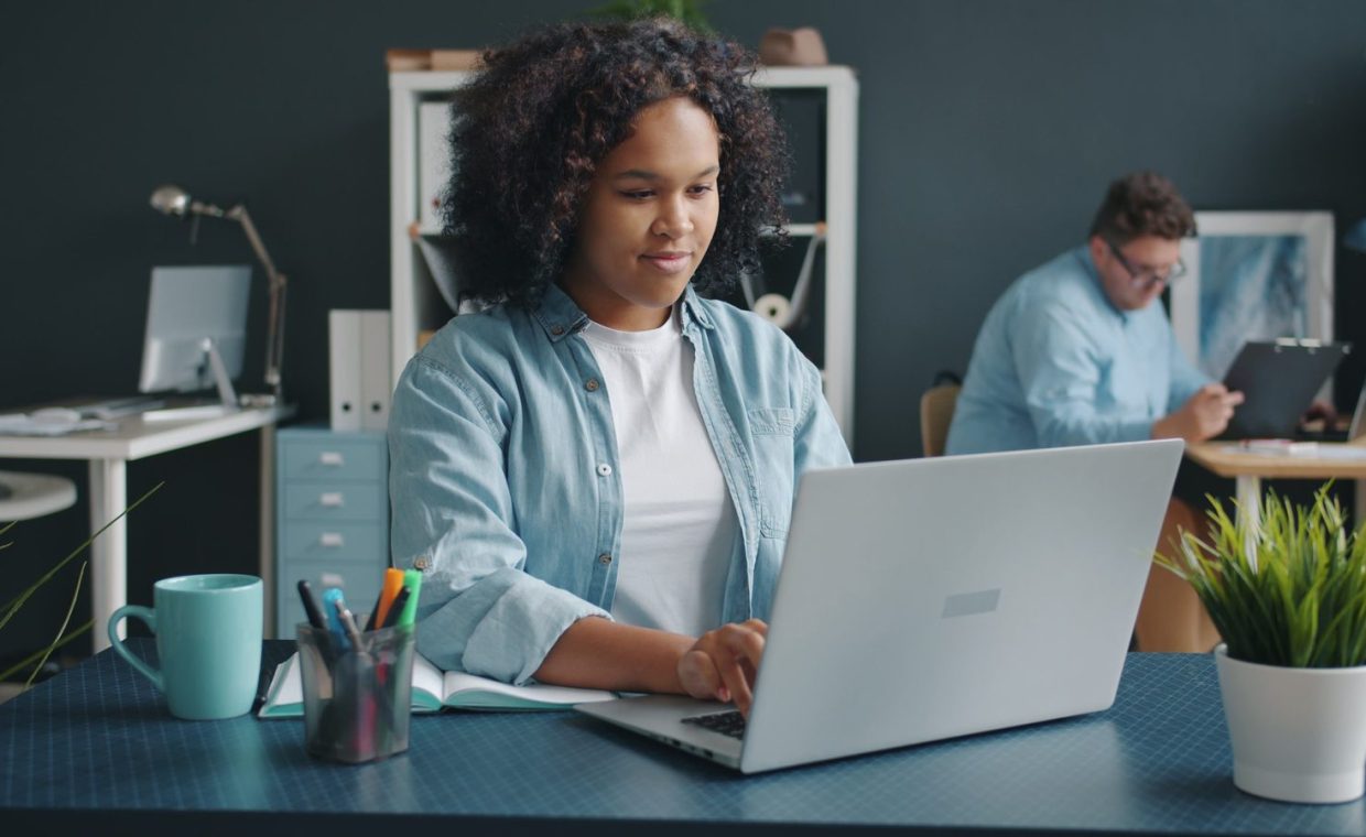 A young woman focused on her laptop in a contemporary office setting, promoting productivity.