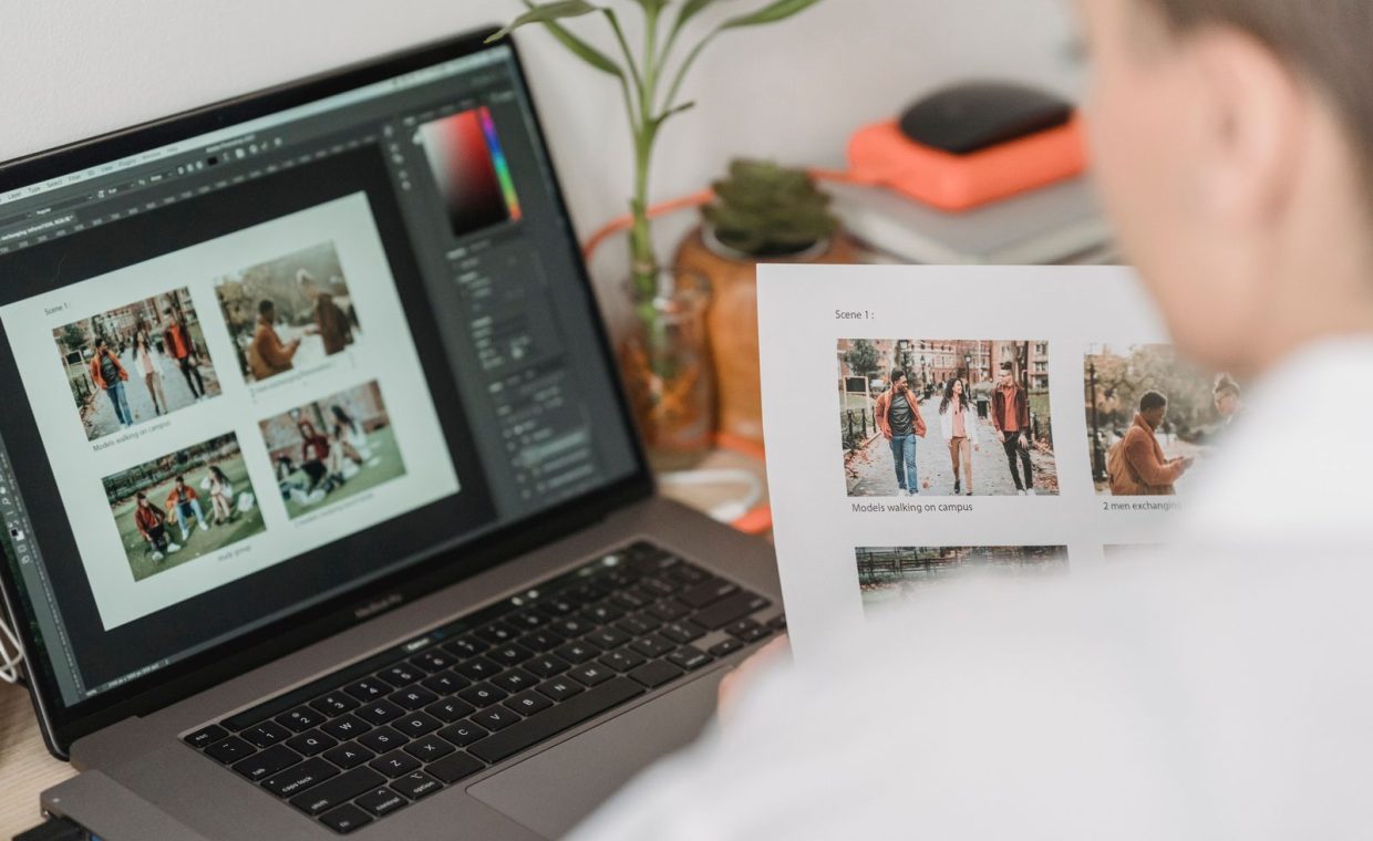 High angle of crop female photographer sitting at table with laptop and printed photoshoot while working remotely