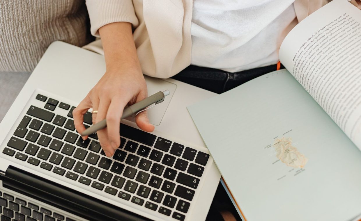 Close-up of a person working on a laptop and reading an open book. Ideal for educational themes.