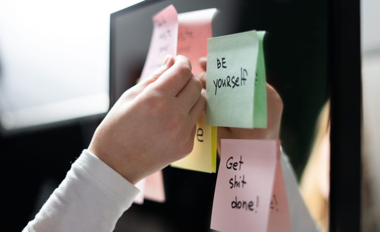 Close-up of hand placing colorful motivational sticky notes on a mirror, inspiring messages.