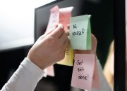 Close-up of hand placing colorful motivational sticky notes on a mirror, inspiring messages.