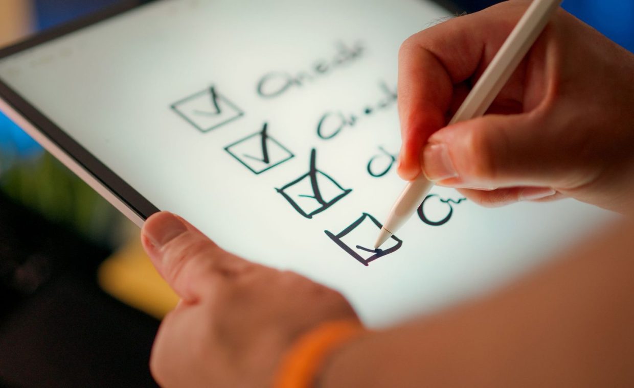 Close-up of a digital checklist being marked off on a tablet with a stylus pen.