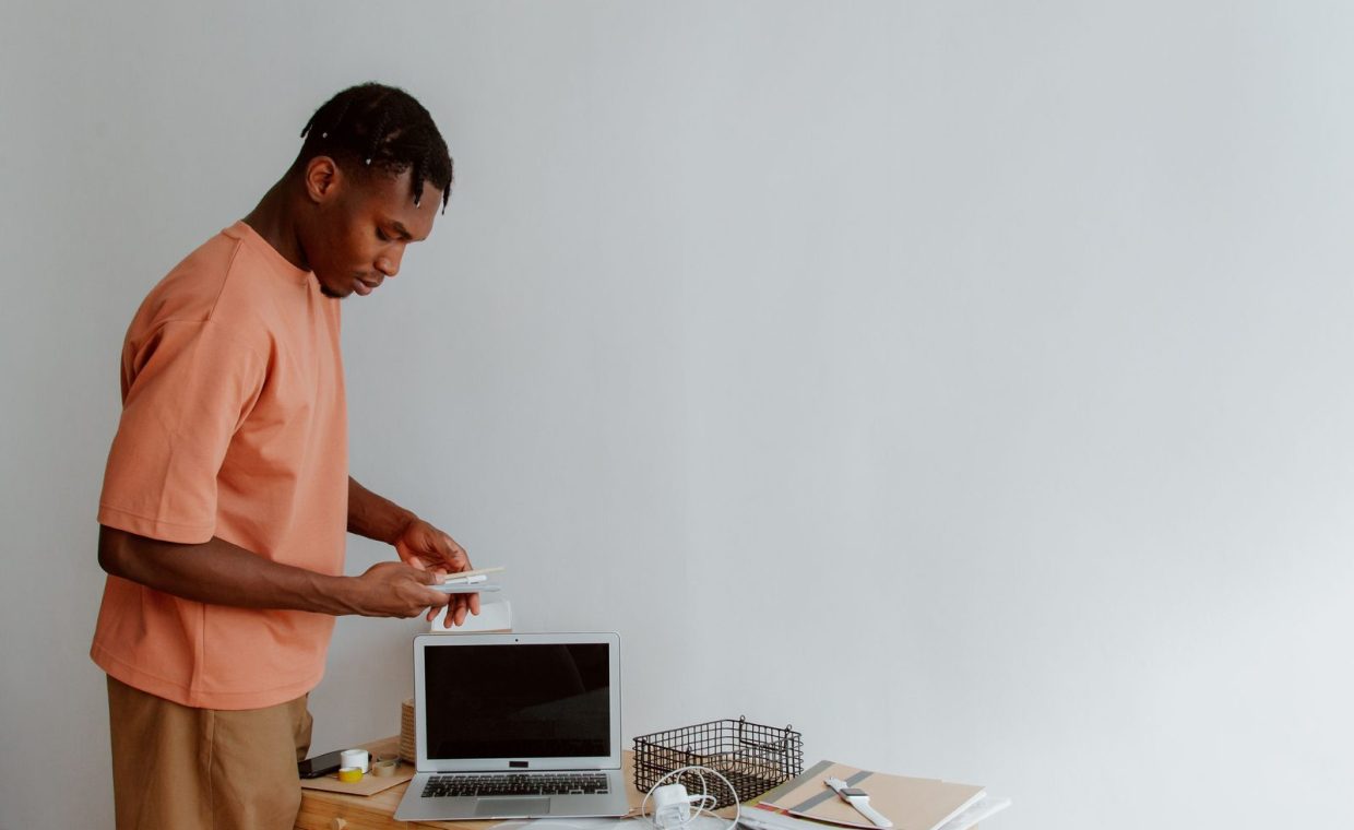 Young man organizing office desk with laptop, notebooks, and supplies in a minimalist workspace.