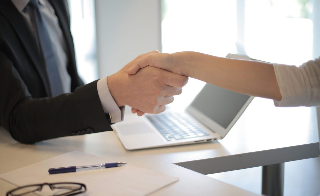 Close-up of a professional handshake over a laptop during a business meeting in an office.