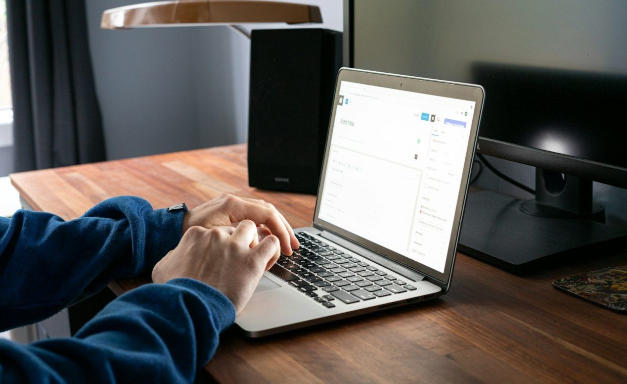 person using macbook pro on brown wooden table