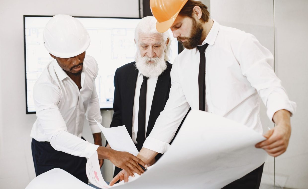 Three architects in office reviewing blueprints, showcasing teamwork and professional attire.