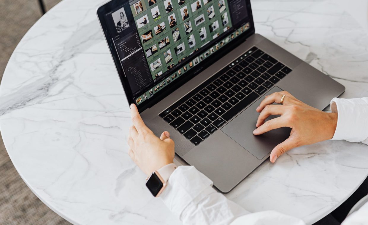 Hands editing photos on laptop, modern workspace on marble table.