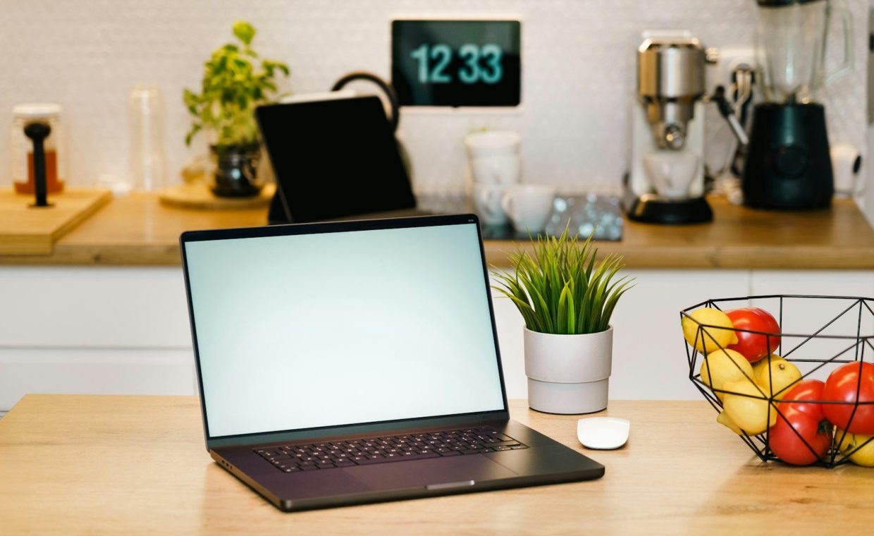 A laptop sits on a kitchen counter workspace.