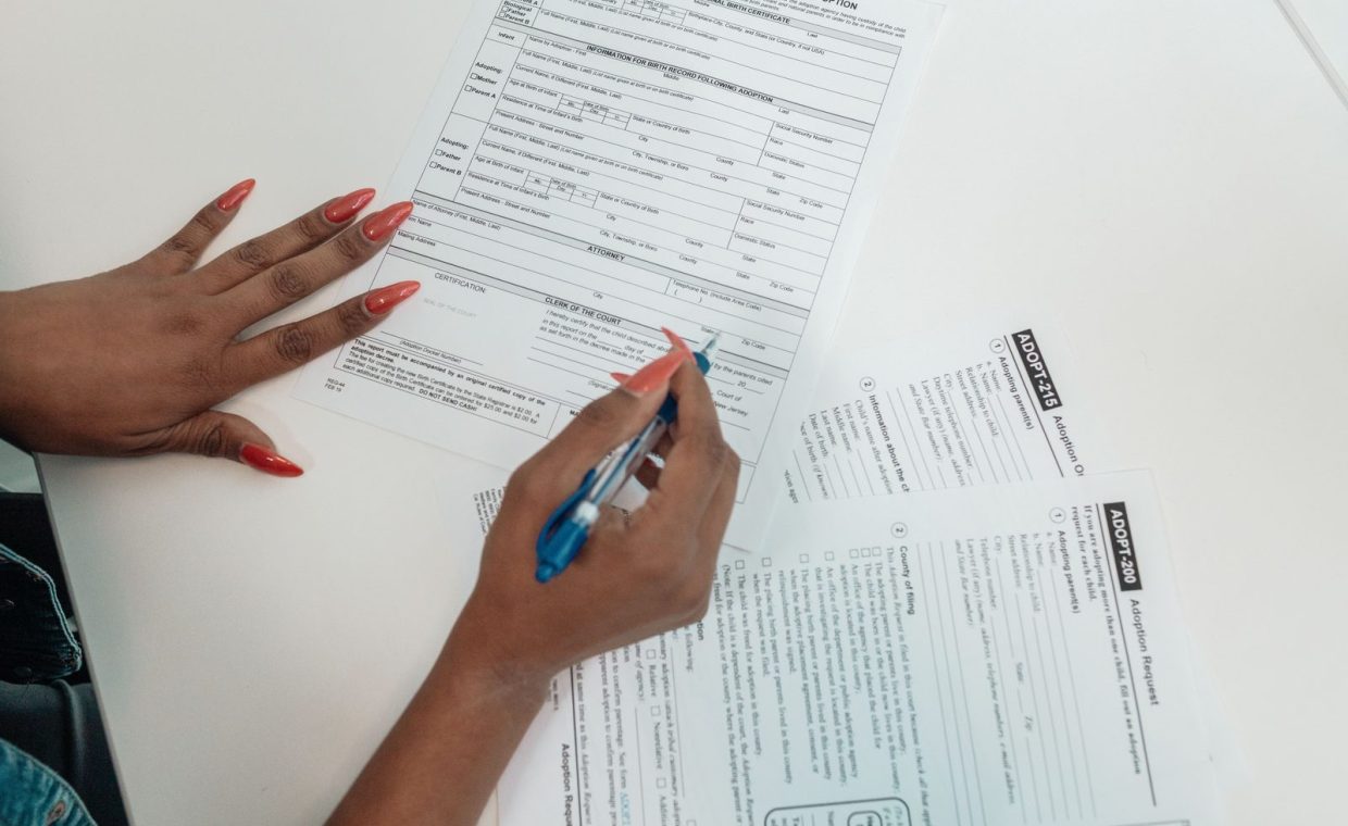 A woman with red nails fills out adoption application forms on a desk.