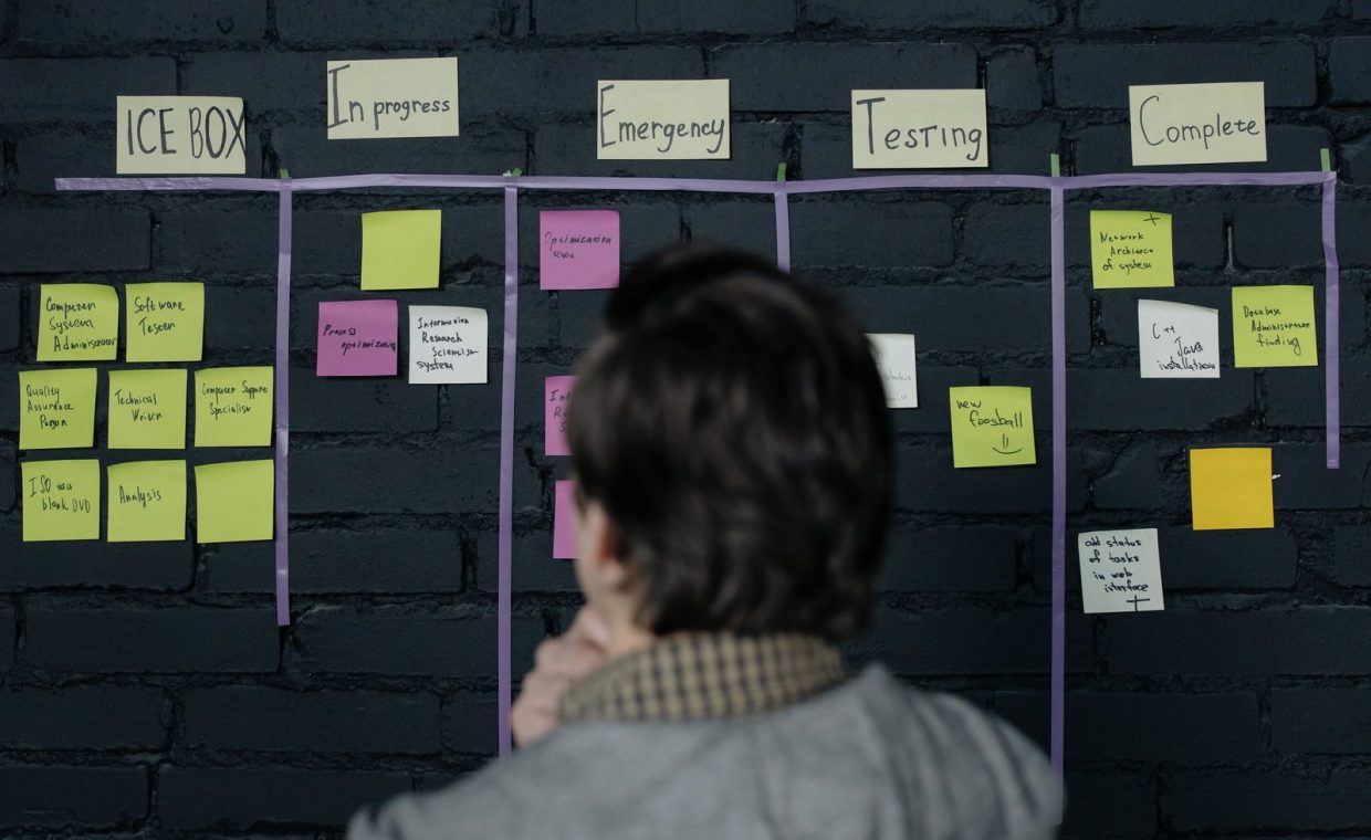 A man in an office reviews a scrum task board filled with sticky notes, planning strategy and organization.