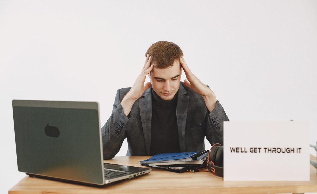 Young man in home office feeling stressed, working during pandemic with motivational message by his side.
