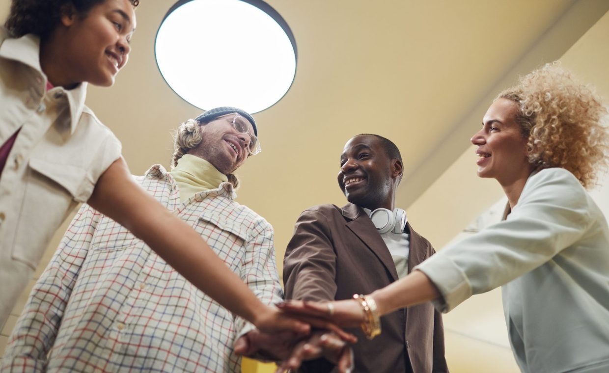 A diverse group of colleagues joyfully engaging in teamwork during an indoor office meeting.