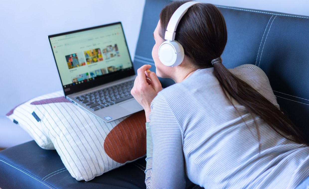 A woman enjoying leisure time with headphones and a laptop on a sofa.
