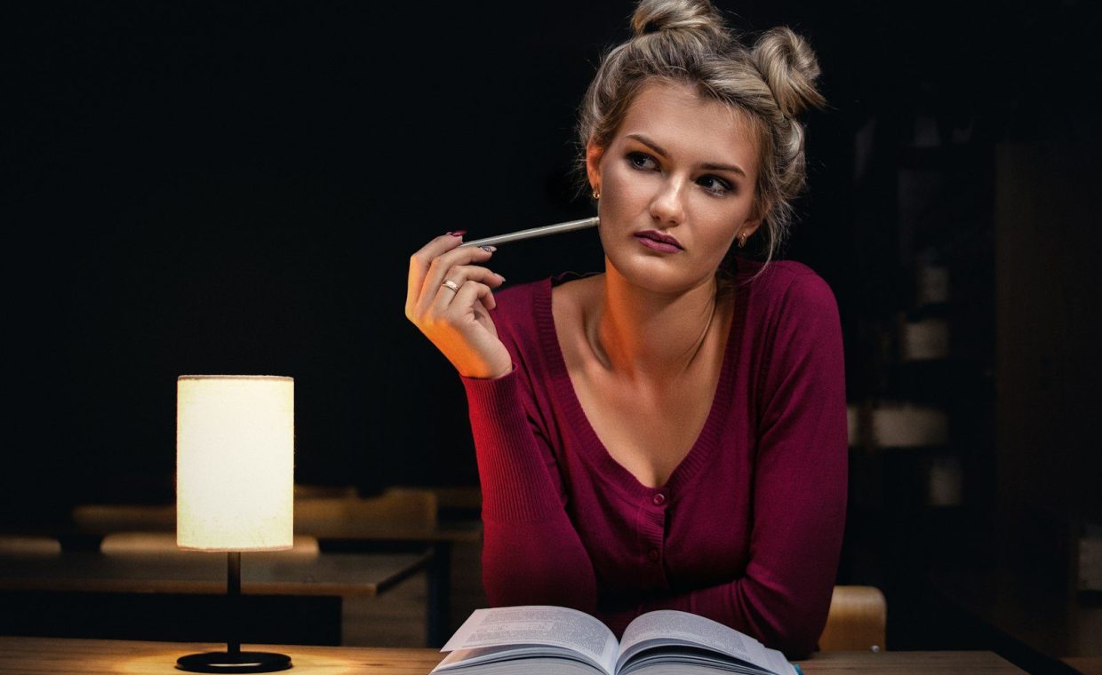 woman sitting beside opened book holding pencil